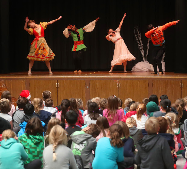 4 children in colorful costumes 'dabbing" on stage while a group of children in the audience looks on